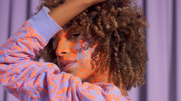 Mujer de raza mixta con cabello rizado y patrón de maquillaje de neón brillante en la cara al igual que en su sudadera