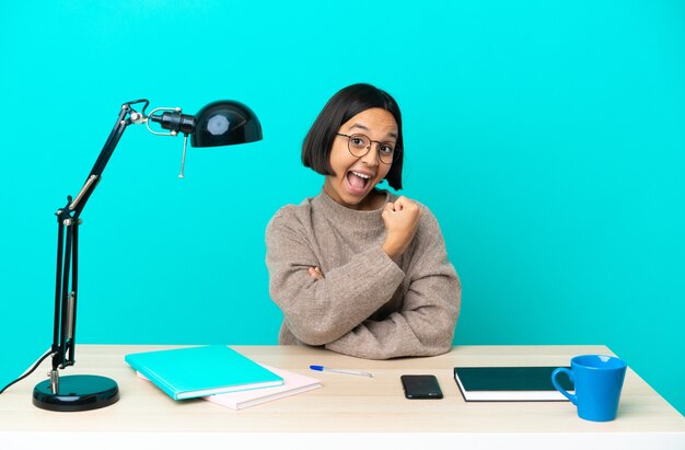 Mujer de raza mixta joven estudiante estudiando en una mesa celebrando una victoria