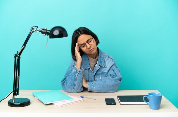 Mujer de raza mixta joven estudiante estudiando en una mesa con dolor de cabeza