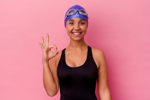 Mujer de raza mixta joven nadador aislada en pared rosa alegre y confiado mostrando gesto ok