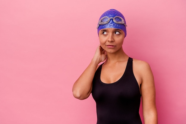 Mujer de raza mixta joven nadador aislada en pared rosa tocando la parte posterior de la cabeza, pensando y haciendo una elección