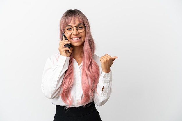 Mujer de raza mixta de negocios joven con cabello rosado sosteniendo un móvil aislado sobre fondo rosa apuntando hacia el lado para presentar un producto