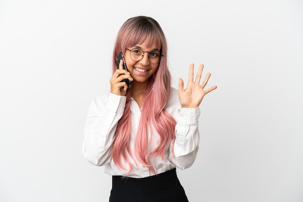 Mujer de raza mixta de negocios joven con cabello rosado sosteniendo un móvil aislado sobre fondo rosa contando cinco con los dedos