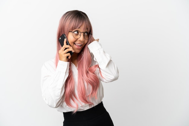 Mujer de raza mixta de negocios joven con cabello rosado sosteniendo un móvil aislado sobre fondo rosa escuchando algo poniendo la mano en la oreja