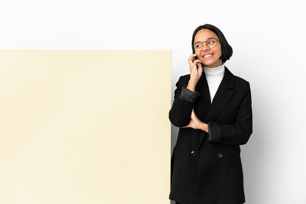 Mujer de raza mixta de negocios joven con una gran pancarta sobre antecedentes aislados manteniendo una conversación con el teléfono móvil