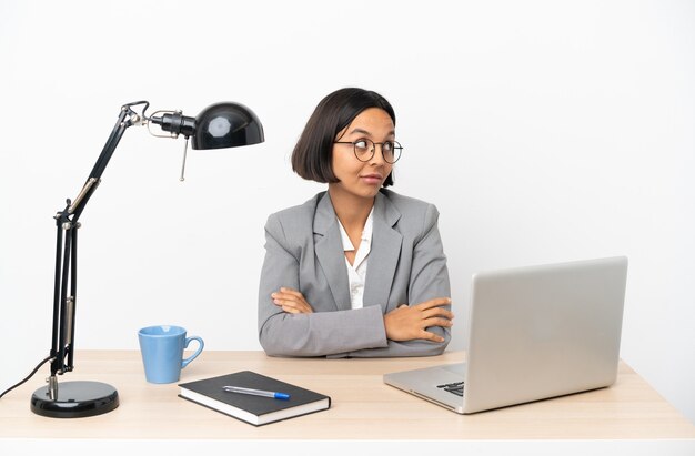 Mujer de raza mixta de negocios joven que trabaja en la oficina haciendo gesto de dudas mirando de lado