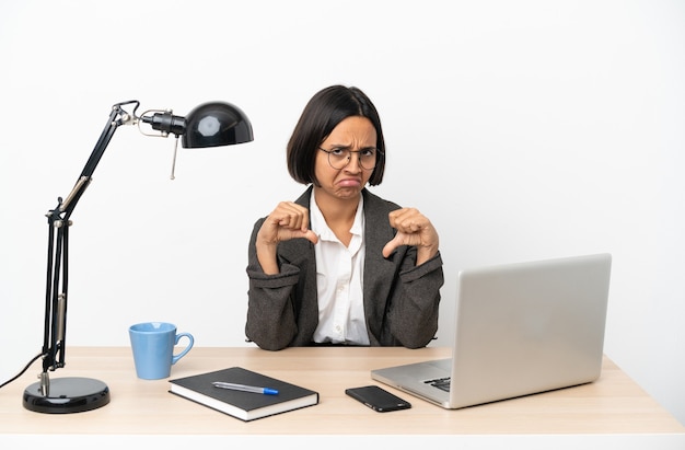 Mujer de raza mixta de negocios joven que trabaja en la oficina mostrando el pulgar hacia abajo con las dos manos