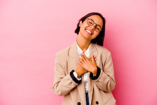 Mujer de raza mixta de negocios joven en rosa riendo manteniendo las manos en el corazón, concepto de felicidad.