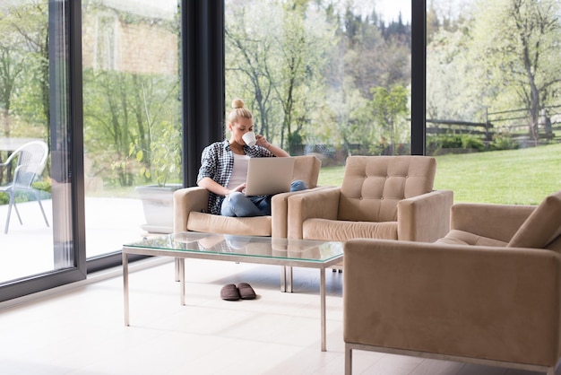 Mujer real que usa la computadora portátil en casa tomando café disfrutando de relajarse