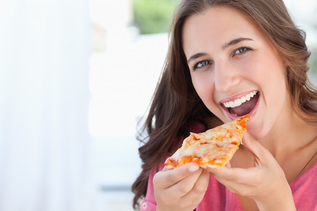 Una mujer con una rebanada de pizza en sus labios
