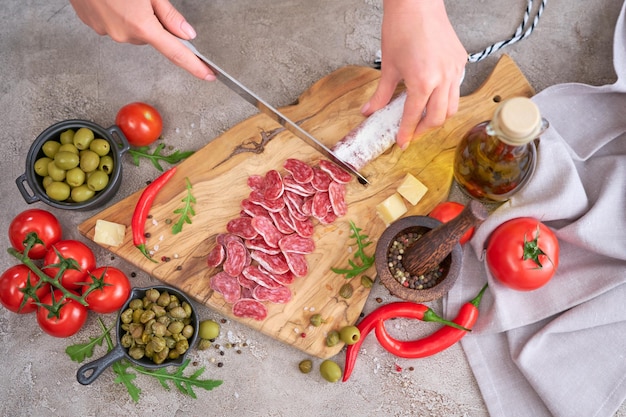 Mujer rebanar salchicha española fuet salami con cuchillo en una cocina doméstica