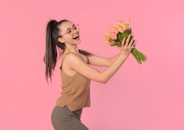 mujer recibe flores sostiene un hermoso ramo y se ríe felizmente fondo rosa