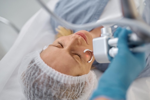 Mujer recibiendo un procedimiento cosmético de limpieza facial con láser en la vista del salón de belleza desde arriba. Tratamiento profesional de la piel