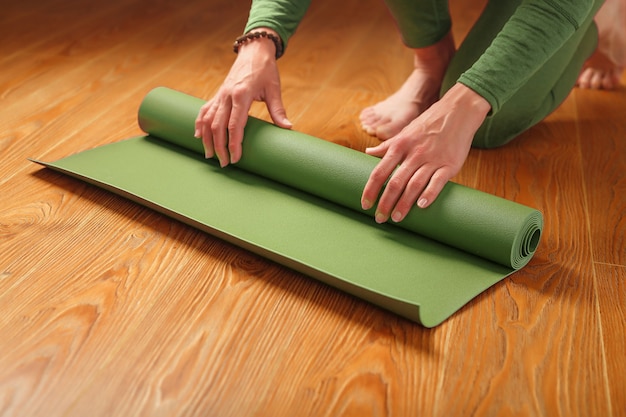 Una mujer recoge una alfombra verde después de una clase de yoga.