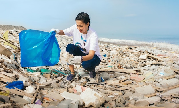 Una mujer recoge basura en una playa. copia espacio