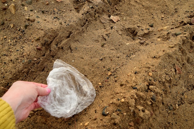 La mujer recoge una bolsa de plástico en la arena cerca de la contaminación de la orilla del río y el medio ambiente Concepto de ecología