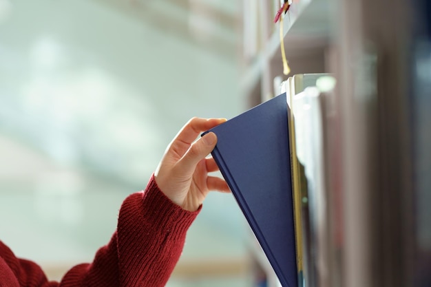Mujer recogiendo a mano el libro de la estantería en la biblioteca en la escuela secundaria universitaria o en la librería