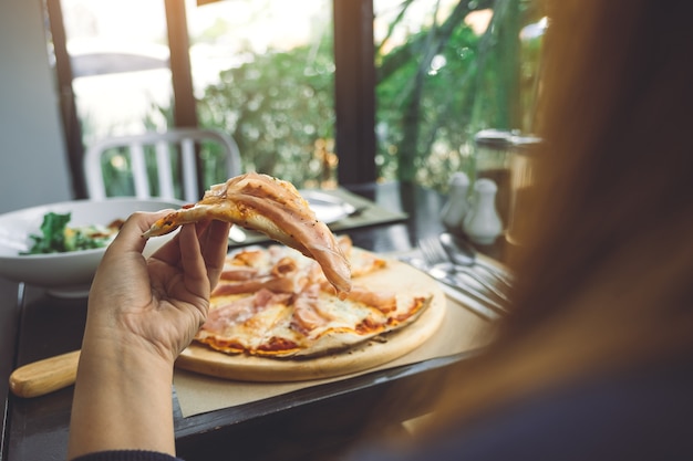 una mujer recogiendo un pedazo de pizza de jamón de Parma para comer en el restaurante