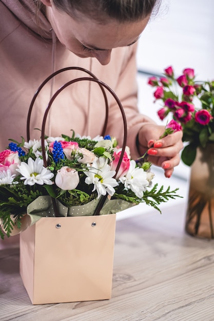 Mujer recogiendo ramo de flores diferentes en bolsa de regalo de papel con asas. Vertical