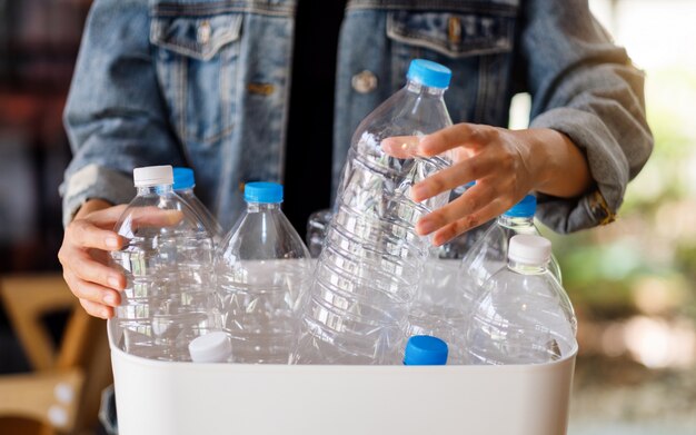 Una mujer recogiendo y separando botellas de plástico de basura reciclable en un contenedor de basura en casa