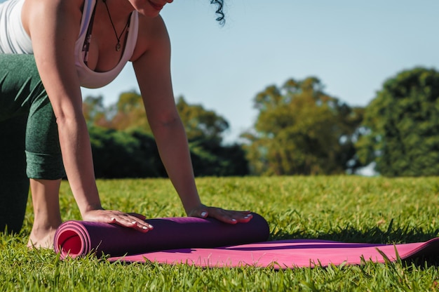 mujer recogiendo su colchoneta de yoga rosa después de una práctica en un concepto de yoga y estilo de vida del parque