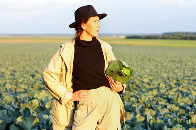 Mujer recogiendo verduras de col en el campo. Granjero de sexo femenino que trabaja en la granja orgánica. Cosecha en otoño.