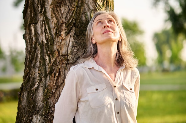 Mujer recostada contra el árbol mirando hacia arriba