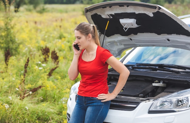 Mujer recostada sobre el coche roto y pidiendo ayuda por teléfono móvil