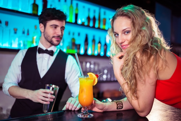 Mujer recostada sobre el mostrador mientras barman en segundo plano.