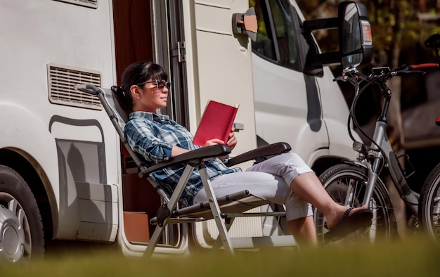 La mujer se relaja y lee un libro cerca del camping. Vacaciones en coche caravana. Viajes de vacaciones familiares, viajes de vacaciones en autocaravana RV.