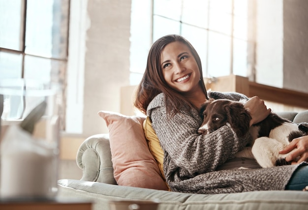 Foto la mujer se relaja en el sofá con una sonrisa de perro y está contenta en casa con una mascota y feliz junto con la paz en la sala de estar felicidad amor por los animales y cuidado con la hembra y el cachorro abrazados en el sofá del apartamento