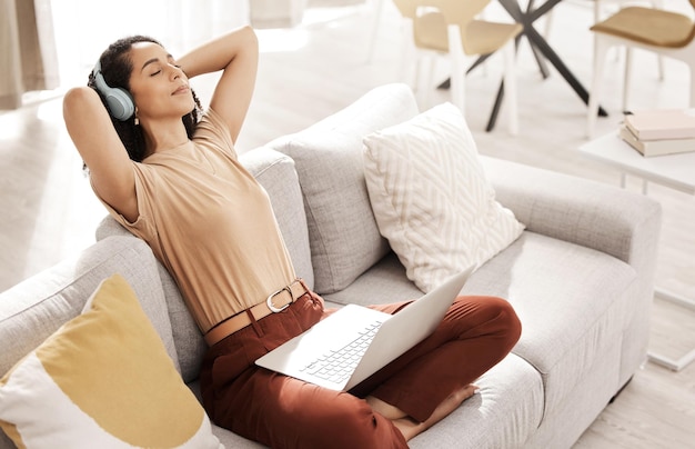 La mujer se relaja y trabaja a distancia con auriculares haciendo investigación de mercado en un sofá de la sala de estar Mujer negra tranquila escuchando música trabajando en Internet con tecnología en paz en casa sintiéndose zen