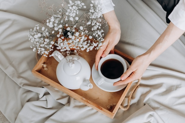 Mujer de relajación por la mañana en la bandeja de la cama con té y flores relajante fin de semana