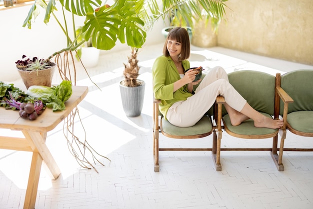 Mujer relajada con comida saludable en la habitación con plantas.