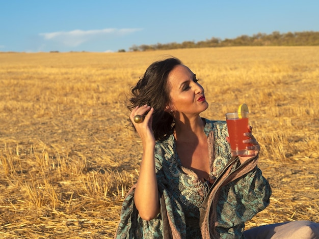 Mujer relajada disfrutando de una bebida fría en el campo de heno