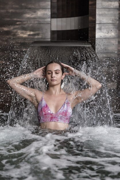 Mujer relajada disfrutando de salpicaduras de agua corriente en el centro de spa