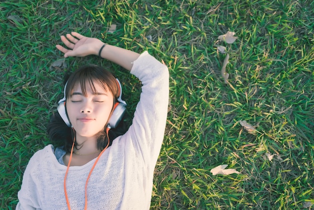 Mujer relajada escuchando música con auriculares tirado en el pasto
