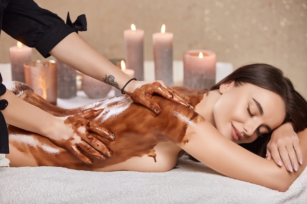 Mujer relajada y hermosa acostada con velas y con procedimientos de esteticista con chocolate en el cuerpo