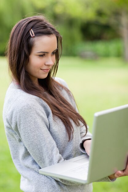 Mujer relajada joven que sostiene su computadora portátil mientras que se coloca en un parque