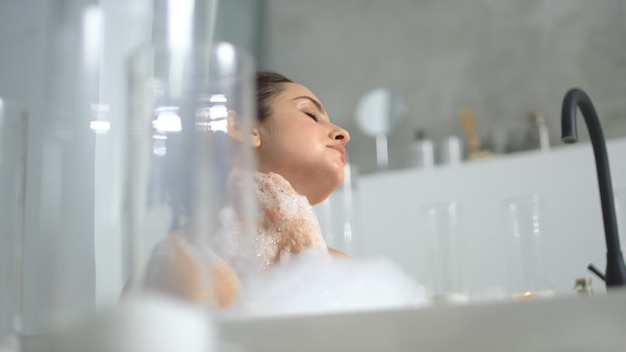 Mujer relajada masajeando el cuello en la bañera Cerrar chica sensual relajándose en baño de espuma Mujer sexy haciendo tratamiento corporal en baño de lujo en cámara lenta
