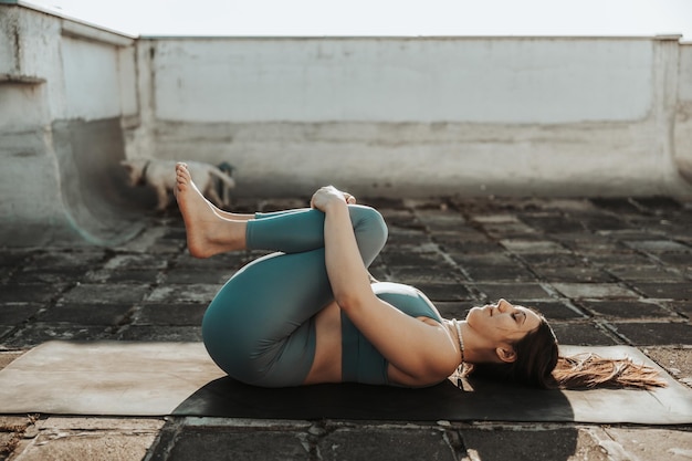 Mujer relajada practicando ejercicios de estiramiento de yoga en una terraza en la azotea.