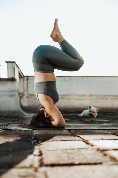 Mujer relajada practicando el soporte de cabeza de yoga en una terraza en la azotea.