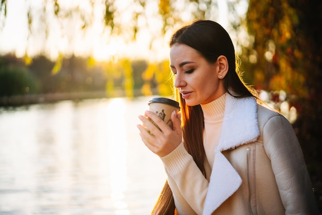 Mujer relajada que huele a café Señora en el parque de otoño con taza de café