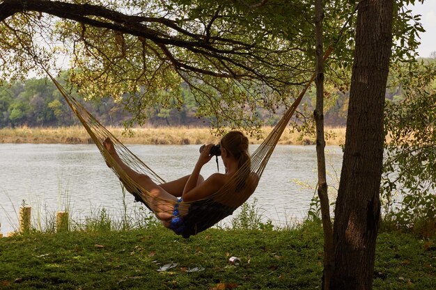 Foto mujer relajándose en una hamaca mirando a través de binoculares en la orilla del lago