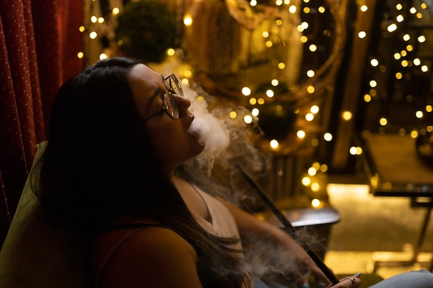 Foto mujer relajándose vaping de una pipa de agua en un bar.