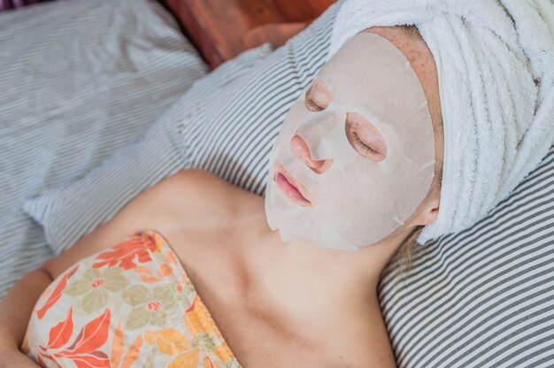 mujer relajante en la cama con una máscara facial