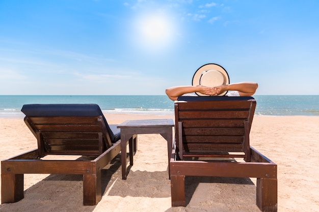 Mujer relajante en silla de playa o terraza con vistas al mar en la playa