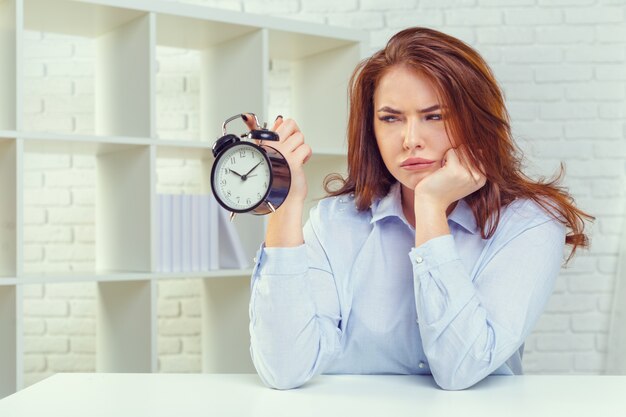 Mujer con reloj despertador en la mesa en la oficina