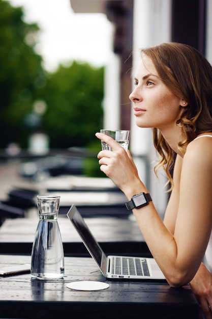 Mujer con relojes inteligentes bebiendo un vaso de agua en la cafetería de verano