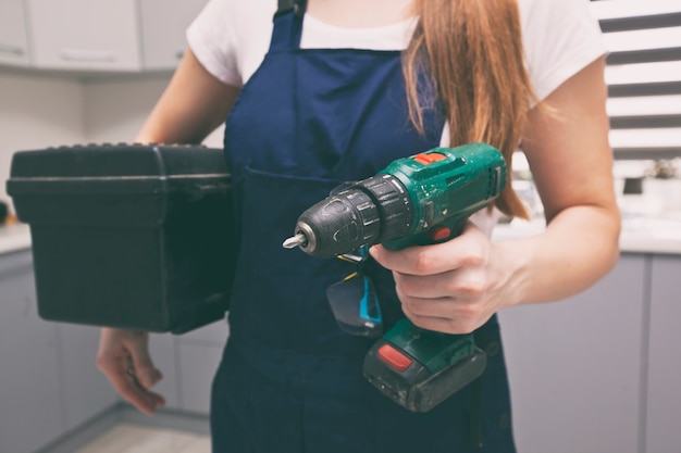 La mujer reparadora vestida con uniforme de trabajo en la casa con caja de herramientas y otros equipos en la mano